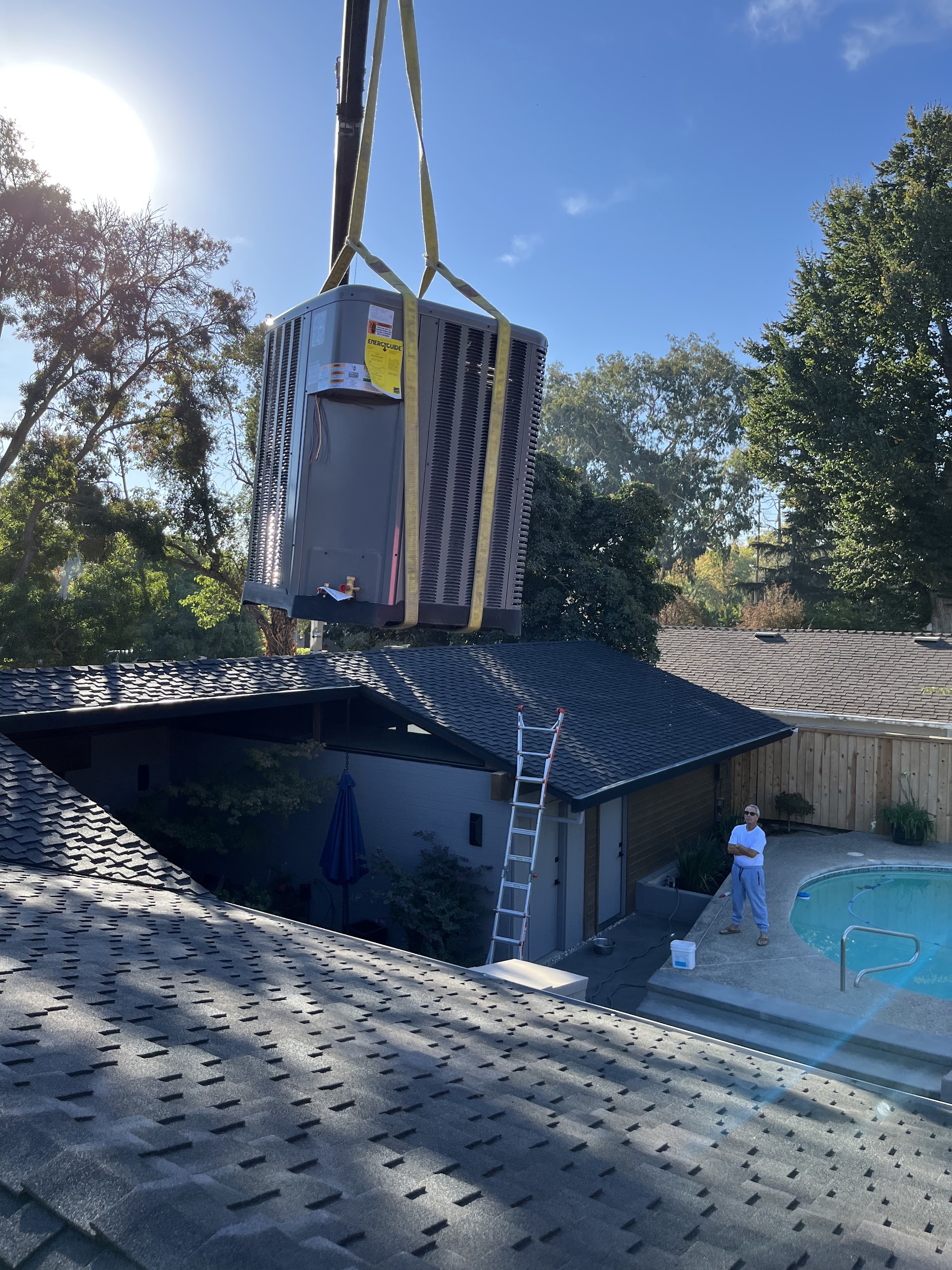 Crane lifting a new condenser unit onto a rooftop by a pool